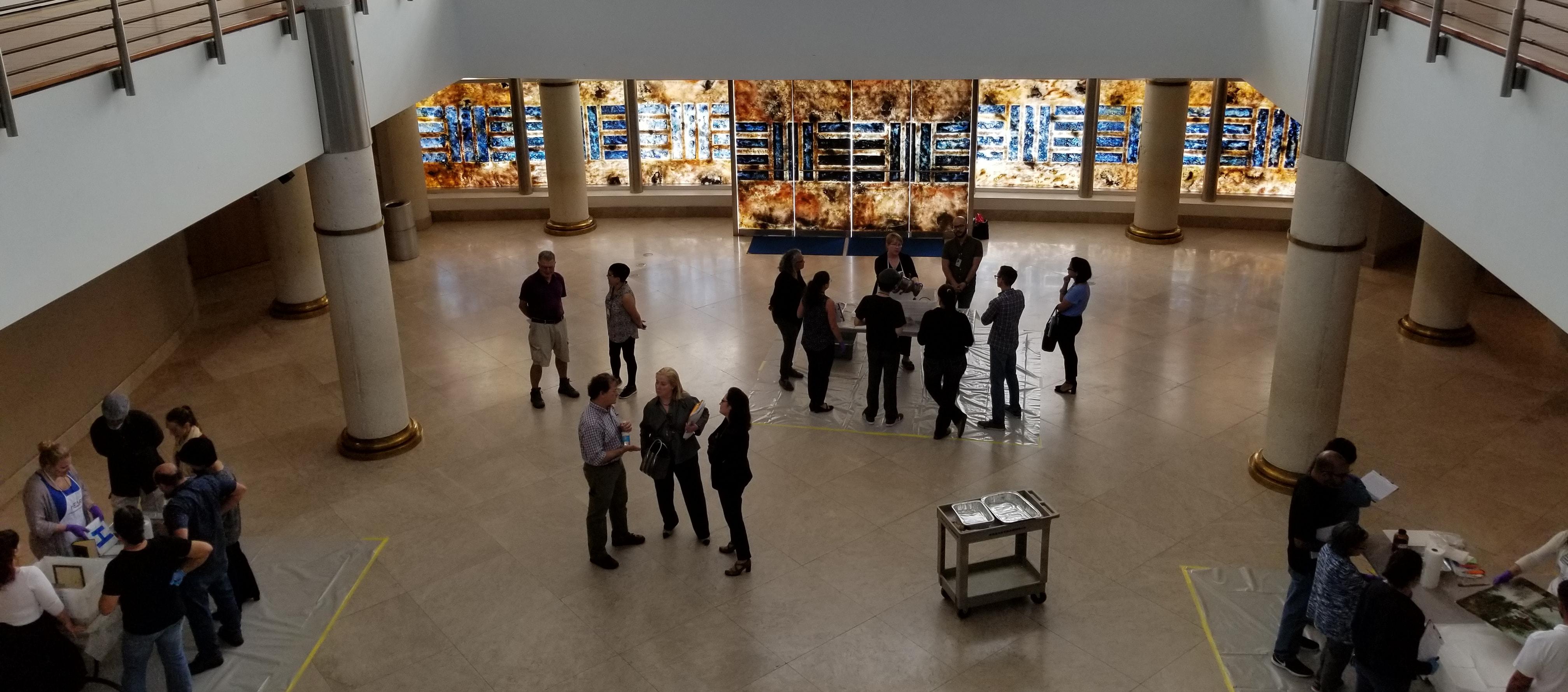 People in large atrium crowding around tables with objects