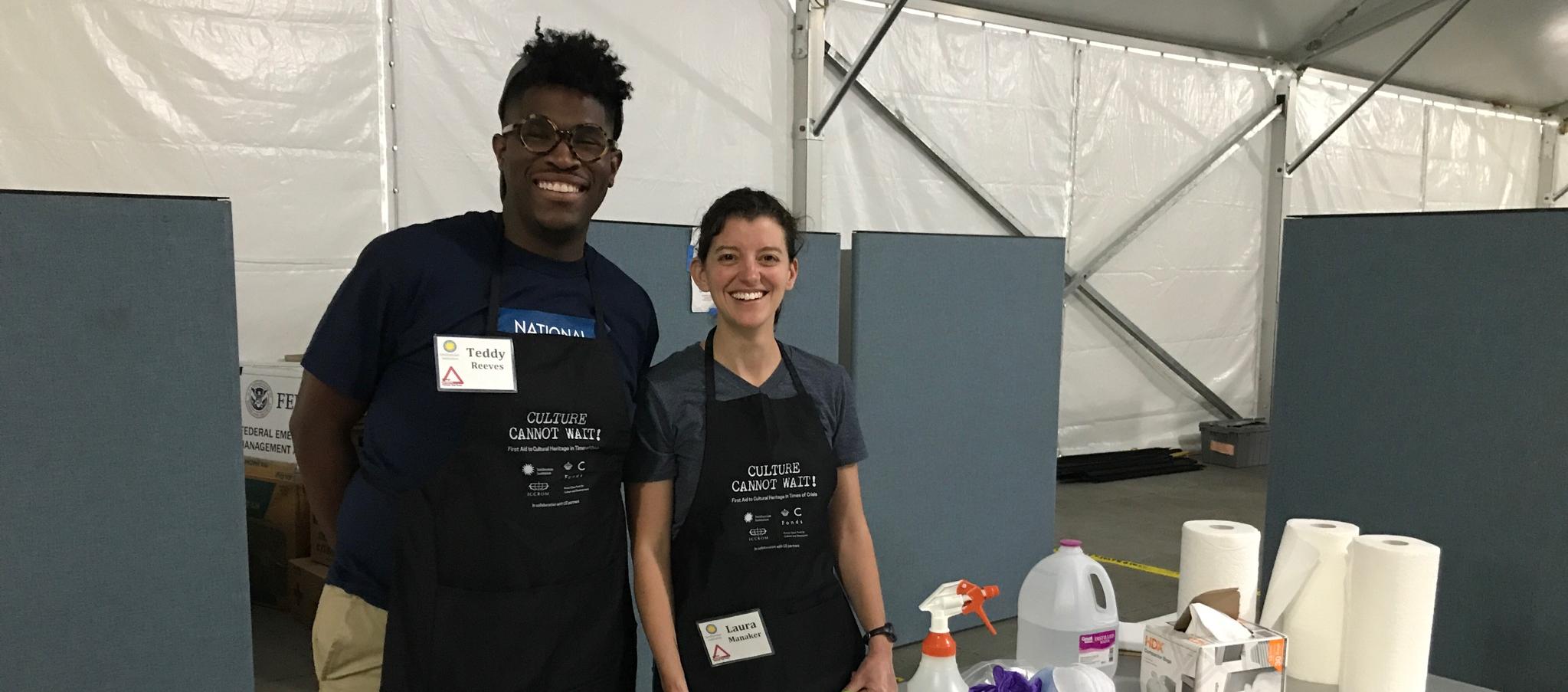 a man and a woman stand behind a table set up with conservation materials.