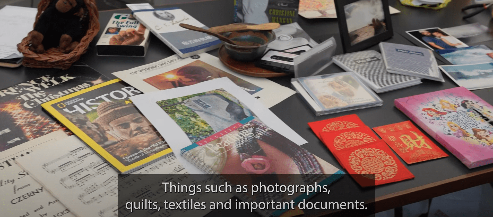 Table of books, magazines, photographs.  Text reads: Things such as photographs, quilts, textiles and important documents