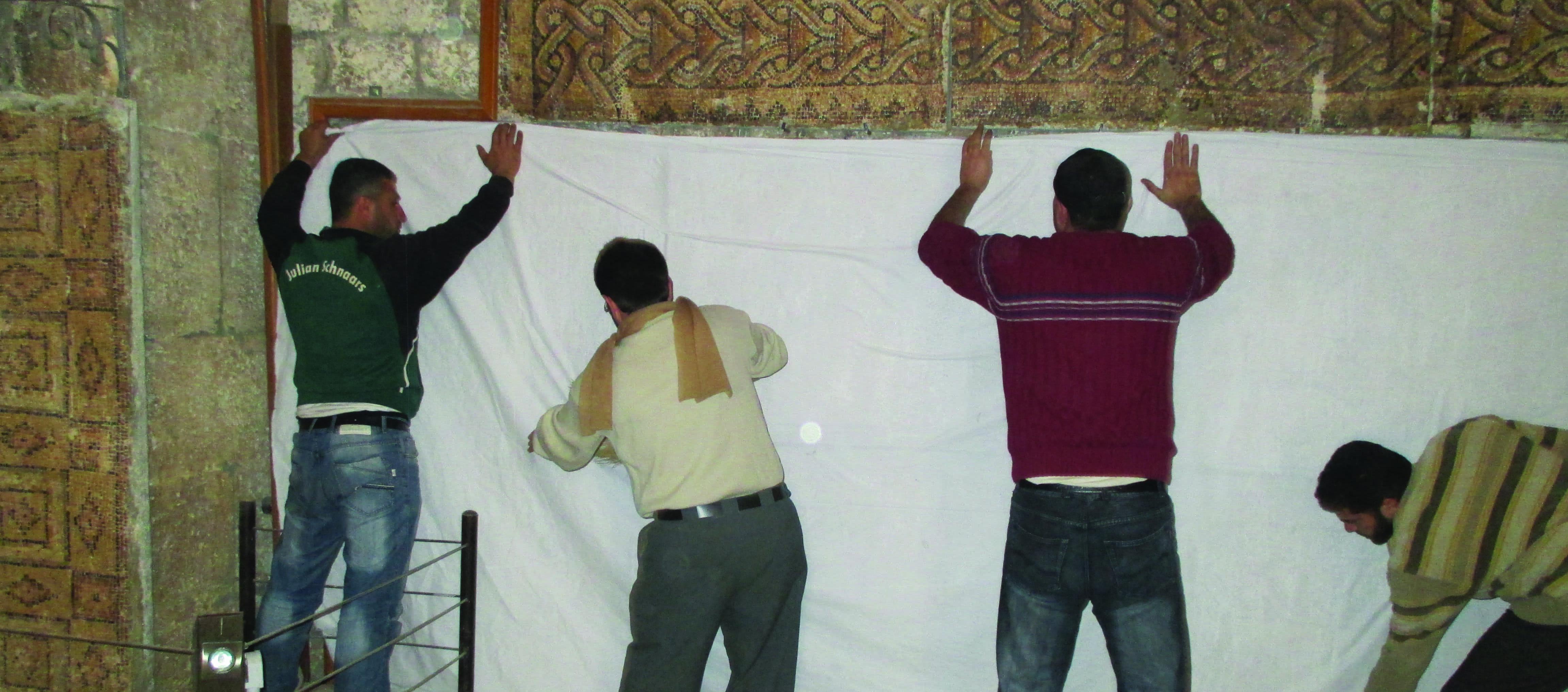 four men cover a mosaic with a white cloth