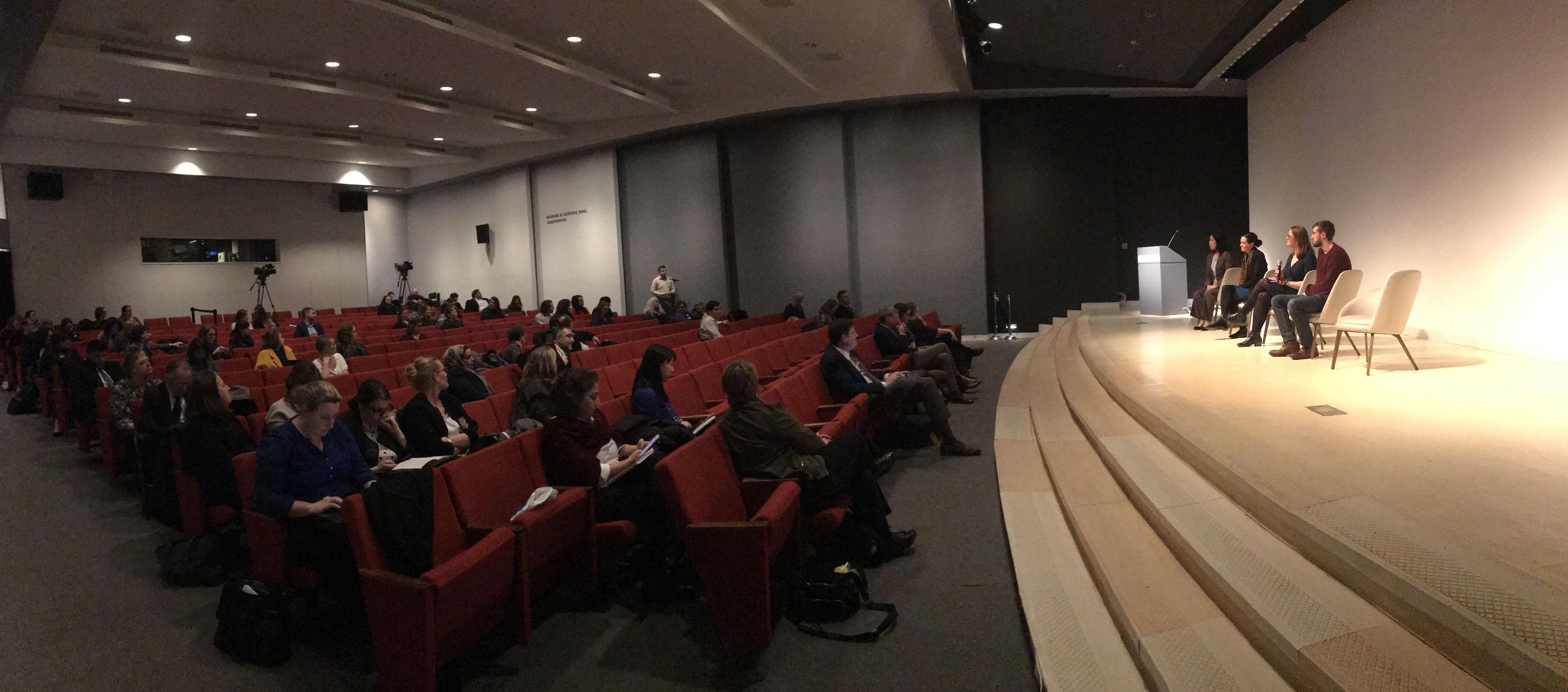 a panel of speakers sit on stage crowd looks on.