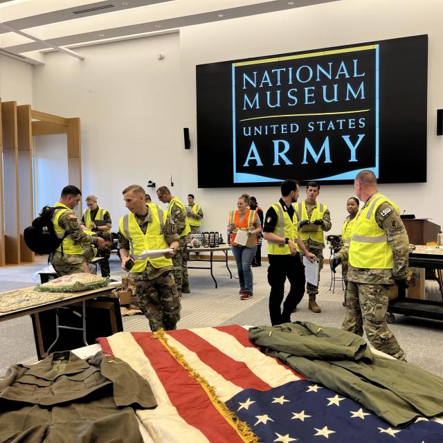 Men and women in military uniform and yellow vests.  American flag in foreground and National Museum of the United States Army sign in backgroud