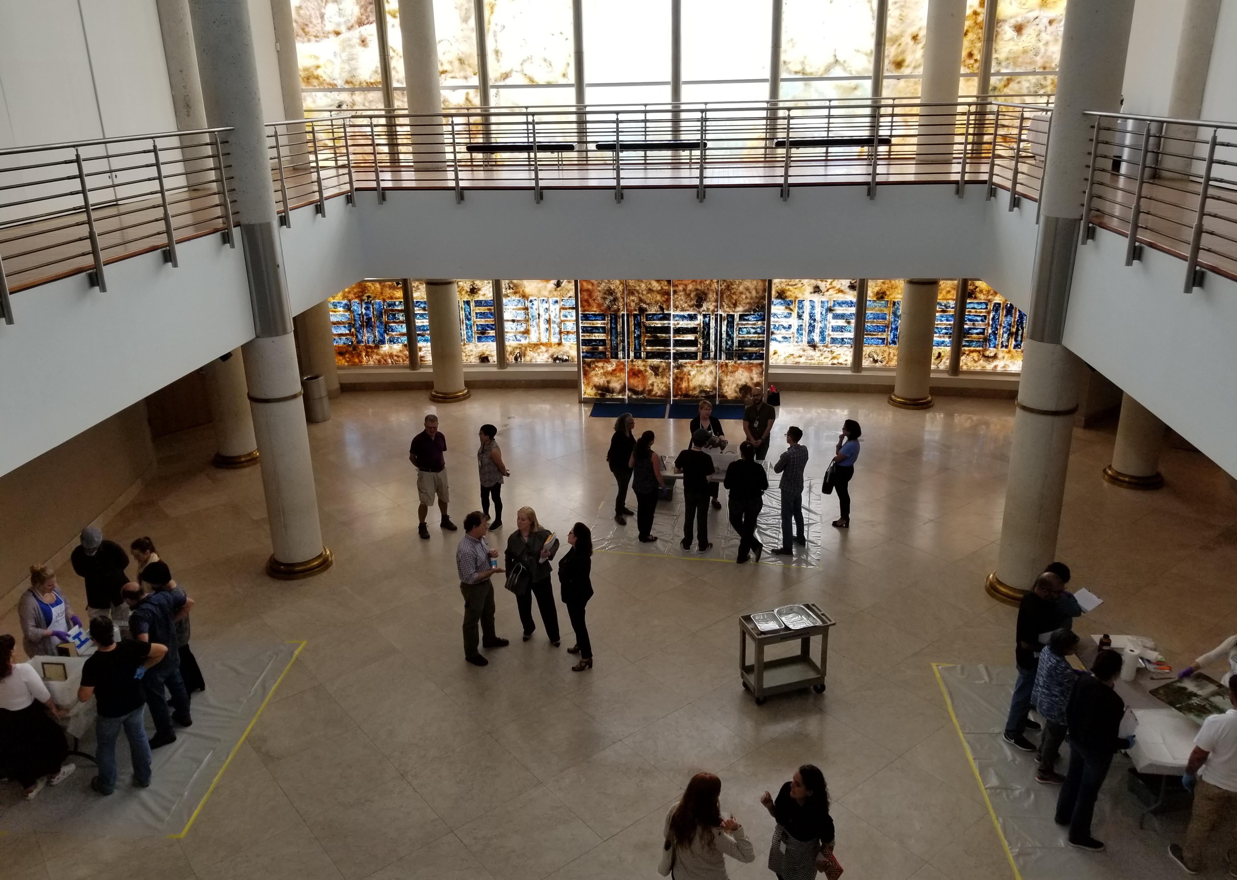 People in large atrium crowding around tables with objects